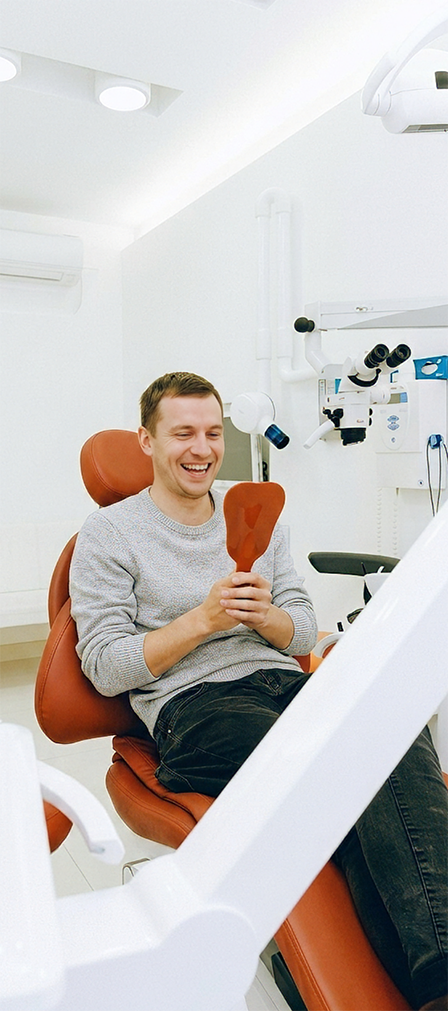 Young man in the dental chair smiling at his reflection